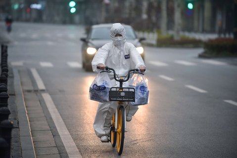 Ein Anwohner trägt einen Schutzanzug, während er mit dem Fahrrad durch Wuhan, China, fährt. 