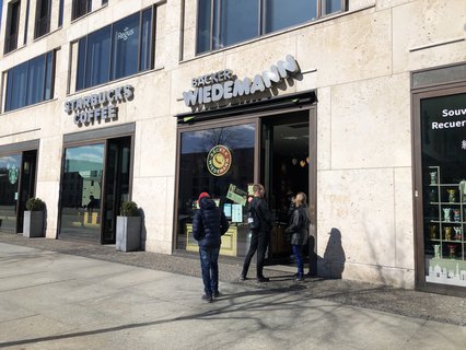 Ein paar Menschen stehen beim Bäcker an.