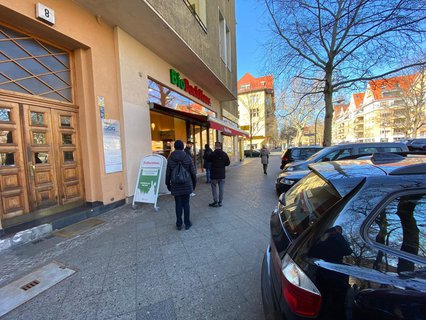 Wenige Menschen warten in der Schlange vor einem Bäcker am Rüdesheimer Platz.