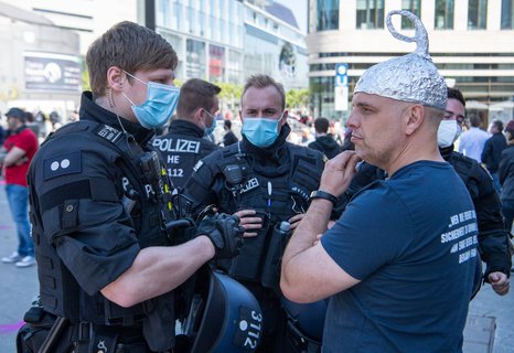 Polizisten erteilen am Rande einer Demo in Frankfurt einem Mann mit Aluhut einen Platzverweis.