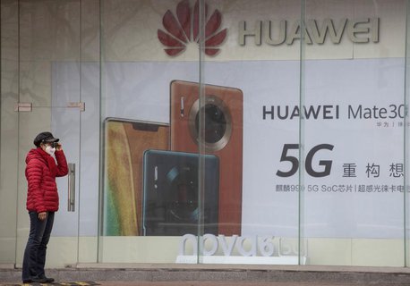 Eine Frau mit Mundschutz steht vor einer Werbung für Smartphones von Huawei. 