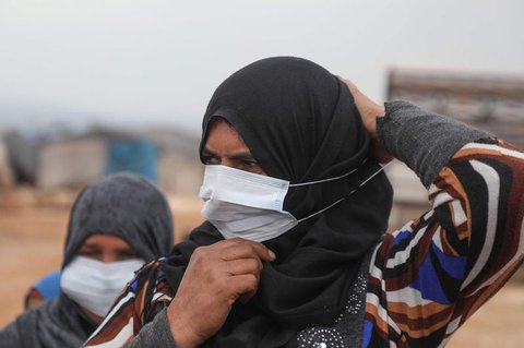 Eine Frau in einem Flüchtlingslager setzt eine Maske auf.