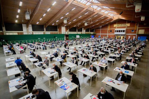 Teilnehmer des Landesparteitags der Berliner AfD sitzen in einer Halle des MAFZ-Erlebnisparks an Einzeltischen.