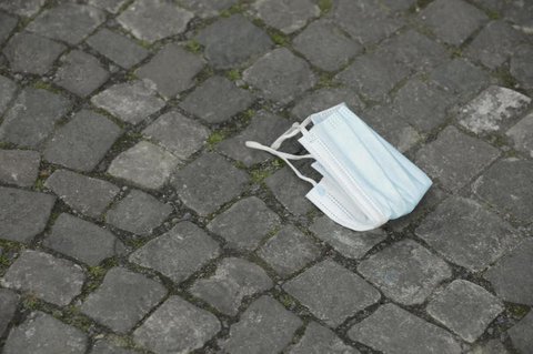 Eine getragene Maske liegt auf dem Plaster.