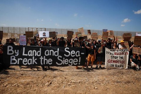 Menschen halten Schilder und Transparente hoch, während sie an einer Protestkundgebung an der Grenze zwischen Israel und dem Gazastreifen teilnehmen.