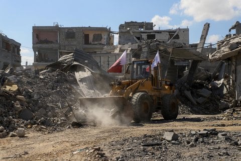 Ein Bagger, auf dem unter anderem die katarische Flagge weht, entfernt in Gaza-Stadt Trümmer.