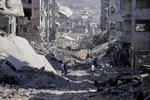 Palästinenser gehen zwischen zerstörten Gebäuden in Gaza-Stadt eine Straße entlang.