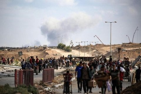 Im Hintergrund steigt eine Rauchwolke auf, während Palästinenser von einer Lebensmittelausgabestelle der von den USA und Israel unterstützten Organisation Gaza Humanitarian Foundation (GHF) in der Nähe des Netsarim-Korridors im zentralen Gazastreifen am 5. Oktober 2025 zurückkehren (Symbolbild).