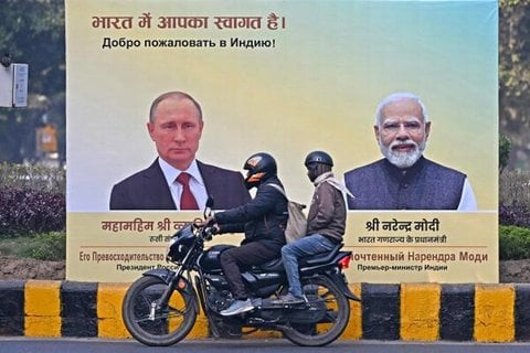 Motorradfahrer fahren am 4. Dezember 2025 in Neu-Delhi an einer Plakatwand mit Porträts des russischen Präsidenten Wladimir Putin und des indischen Premierministers Narendra Modi vorbei.