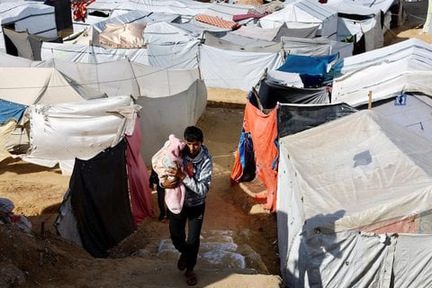 Ein Palästinenser trägt ein Kleinkind durch ein Zeltlager in Deir Al-Balah.