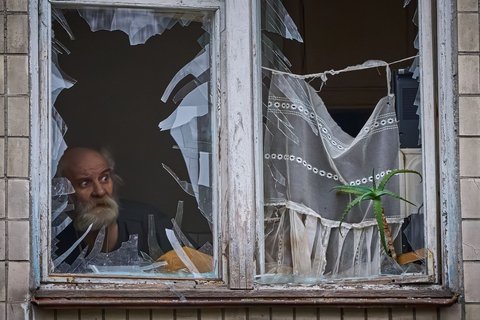 Ein älterer Mann schaut ebenfalls aus seinem zerbrochenen Fenster, als das Wohnhaus in der ukrainischen Hauptstadt getroffen wird. 