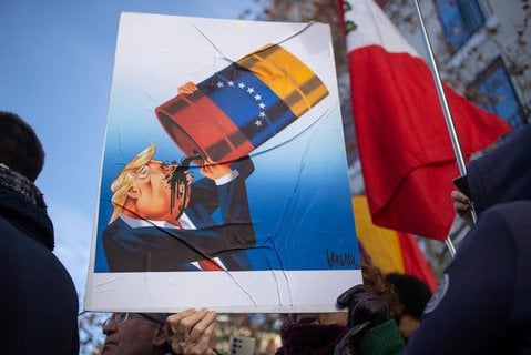Linke Gruppen in Madrid protestieren gegen den US-Angriff in Venezuela. Auf einem Plakat ist dabei eine Karikatur zu sehen, auf der US-Präsident Donald Trump venezolanisches Öl trinkt.  
