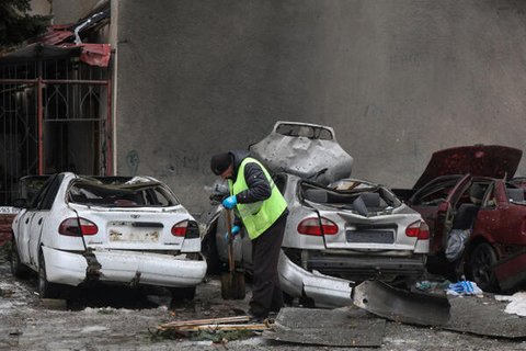 Ein städtischer Arbeiter entfernt Trümmer neben beschädigten Autos vor einem Wohnhaus, das bei einem russischen Drohnenangriff auf Charkiw getroffen wurde.