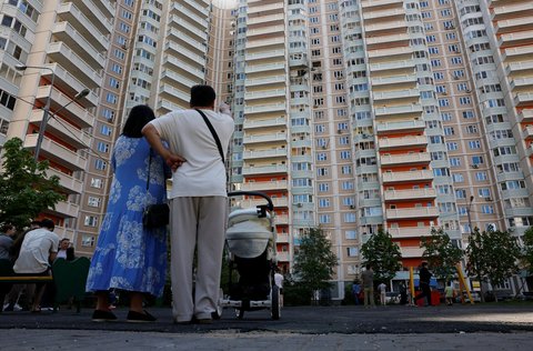 Menschen stehen vor einem Wohnhaus, das bei einem ukrainischen Drohnenangriff in der Region Moskau beschädigt wurde.